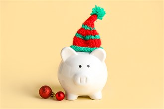 Piggy bank with Christmas hat and baubles on beige background