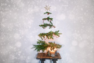 Christmas tree alternative, evergreen branches with decoration hanging on the wall above a rustic wooden stool with candles, sustainable holidays agai