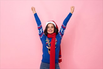 Festive portrait of joyful woman wearing Christmas sweater and hat raising hands up in pink color isolated background studio shot