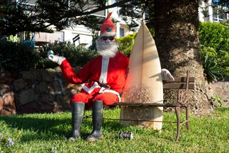 Surfer Santa Claus Surfing Surfie Santa Claus model sitting on garden bench holding surfboard holding can of beer NSW Australia