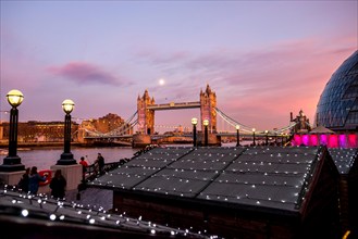 London Tower Bridge at a beautiful full moon evening with Christmas market huts with lights in the foreground.