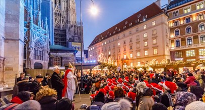 Vienna, Austria, 06th December 2017. St Nicholas (Nikolaus) appears before a crowd of children helpers in traditional red and white Santa hats in the winter festive season Christmas market in Stephans...