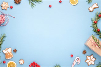 Blue Christmas background made of gigerbread cookies, rosemary branches, berries, gift box, Christmas wreath, cande cane lollipops and rope. Top view.