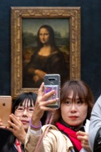 Asian tourists using their smartphones to take selfies with the Mona Lisa painting by artist Leonardo da Vinci, Louvre Museum, Paris, France, Europe