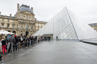 Visitors and tourists queue at the glass pyramid, entrance to the Louvre Museum Paris, France