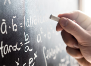 Teacher writing to blackboard with chalk. Student and chalkboard. Professor in school, college or university classroom. Science and education concept.