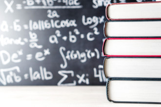 Stack and pile of books in front of a blackboard in school. Math equation handwritten on chalkboard.