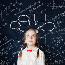 Kids mathematics education concept. Little girl looking up at school blackboard background with hand drawings science formula pattern