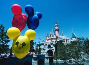 Brightly-colored balloons with the face of Mickey Mouse float in front of Sleeping Beauty Castle, an imposing fairy-tale structure that is the centerpiece of the world’s most famous theme park, Disney...