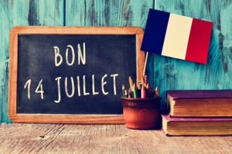 a wooden-framed chalkboard with the text bon 14 juillet, happy 14th of July, the National Day of France, written in French and a
