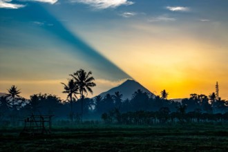 The casts a shadow as it rises over Mt Merapi, an active volcano in Central Java, Indonesia. Smoke spilling from the caldera.