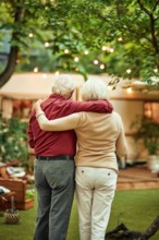Back view of senior married couple looking at their campervan and hugging while standing outdoors. Travel concept
