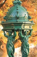 Wallace fountain in Paris by fall / One of the drinking fountains in Paris so called "Wallace fountains" in autumn with yellow foliage as a background