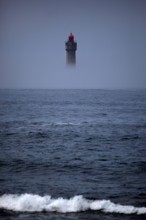 The dramatic La Jument lighthouse, shrounded in summer fog, off the coast of the Ile d'Ouessant, Brittany. The iconic 47-metre high lighthouse was bui