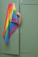 Hand holds to hide rainbow flag back inside closet. Fear of coming out concept. Internalized shame with homosexuality metaphor. LGBT guilt symbol.