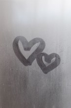 Couple of abstract blurred love heart symbol drawn by hand on the wet window glass with sunlight background. Template for Valentine Day postcards