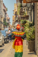 Photograph of a Colombian woman in Cartagena de Indias walking in the Palenqueras dress. Trip to Colombia. Typical colonial colors of the city