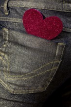 A vibrant red glitter heart-shaped sticker adorns the back pocket of a denim jean, symbolizing casual love and fashion