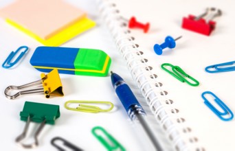 A variety of stationery items, like an eraser, paper clips, and a notebook, are neatly laid out on a clean workspace for school projects.