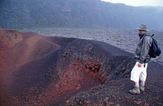 Tourist standing on the edge of Formica Leo crater, Piton de la Fournaise volcano, La Reunion Island, Indian Ocean