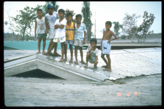 This photograph captures children on a roof in Bamban, Philippines, on December 10, 1991, during the aftermath of the catastrophic eruption of Mount Pinatubo. The eruption caused widespread destructio...