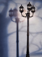 Artistic dramatic photo of a street lamp at night with tree shadow over a white wall