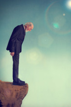 senior elderly man standing alone on a cliff ledge - depression, depressed suicide concept