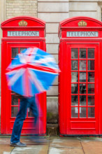 Red London Telephone boxes in the rain with a person holding a Union Jack Umbrella London England UK