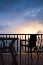 Armchair and table stand on a balcony. Seaside view over bright sunrise sky