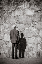 Old man standing in front of stone wall. Sunshine and heavy shadow. Building exterior with copy space.