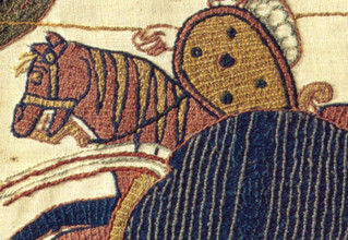 The Bayeux Tapestry, an embroidered cloth from the 11th century, depicts the events leading up to the Norman Conquest of England. This image focuses on a laid work detail of the tapestry.