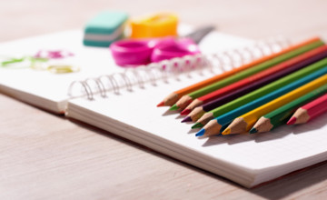 Close up of wooden crayons and other school supplies on blank note book on wooden desk
