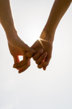 Romantic couple with clasped hands backlit by a bright morning sunburst in a closeup conceptual image of love and friendship.