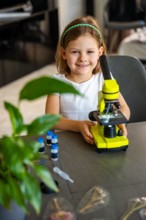 Portrait of little girl with green microscope. Concept of curiosity and early scientific exploration