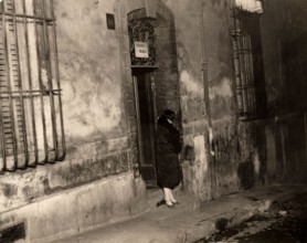 A woman stands by the door of a house in the port city of Marseille, France, in 1929, with a sign reading 'furnished rooms' above the door. Marseille, France, 1929.