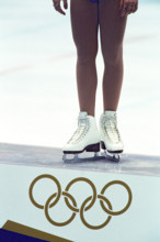 Detail of female figure skater standing atop the podium with the Olympic Rings.