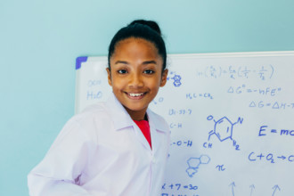 African American girl in lab coat drawing mathematic and science formulas on white board. Creativity and Education concept