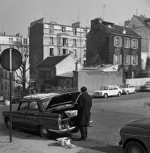 Pariser Bilder [The street life of Paris]  Man at opened trunk, with in the background Cabaret Au Lapin Agile on Rue des Saulfs in Montmartre Date: 1965 Location: France, Paris Keywords : cars, restau...