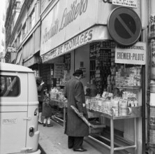 Pariser Bilder [The street life of Paris]  Man with baguette for a dairy store Date: 1965 Location: France, Paris Keywords: groceries, bread, street sculptures, shops, dairy products
