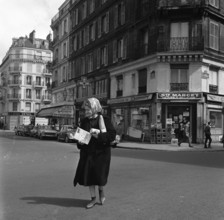 Pariser Bilder [The street life of Paris]  Woman crossing with messages in her hands Date: 1965 Location: France, Paris Keywords: groceries, bread, street sculptures, shops