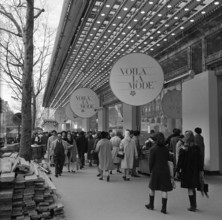 Pariser Bilder [The street life of Paris]  Shopping audience along the display of a clothing store Date: 1965 Location: France, Paris Keywords: clothing, street sculptures, shops