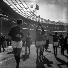 Bobby Moore lifts the Jules Rimet trophy aloft during a lap of honour in Wembley Stadium as the England football team win the FIFA World Cup of 1966, Geoff Hurst, Gordon Banks and Roger Hunt all close...