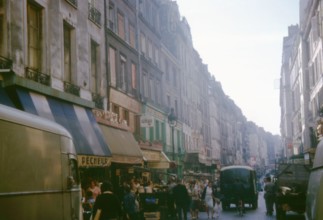 Busy market day on Rue Beaubourg, Paris, France, with shoppers and vintage vehicles. Photographed in September 1964.