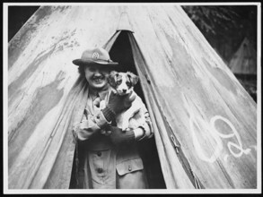 A worker at a World War I camp takes responsibility for the camp's mascot, reflecting the role of morale-boosting activities during wartime.