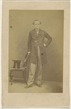 man standing, holding chair back with top hat in seat; about 1865; Albumen silver print