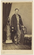 man with moustache standing, holding top hat in one hand, the other hand on chair back; F.W. Baker, British, active Calcutta