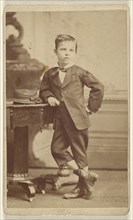 Young boy in suit standing and posed near a table with a hat on top; McClain, American, active 1880s, about 1865; Albumen