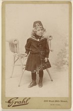 Little girl standing near a chair, wearing a fez; Grahl, American, active New York, New York 1880s - 1890s, about 1890; Gelatin