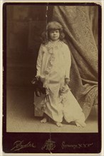 Ethel Butter in white dressing gown, holding pair of shoes and a doll, standing; Philip S. Ryder American, active 1870s - 1920s