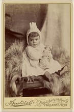 Baby girl in bonnet, seated, holding a doll; A. Husted & Company; about 1880; Albumen silver print